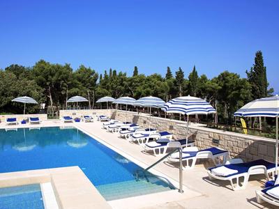 Poolbereich mit Liegestühlen und Sonnenschirmen neben einem großen Außenpool und begrünter Umgebung.