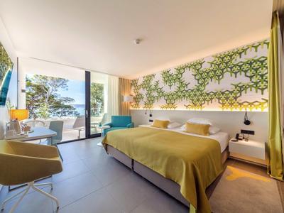 Modernes Hotelzimmer mit großem Bett, Sitzbereich und Blick auf Terrasse und Meer.