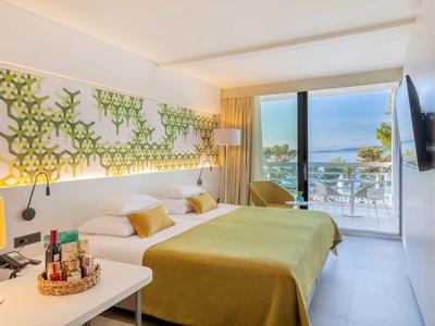 Licht hotelkamer met tweepersoonsbed, balkon met zeezicht en modern meubilair.