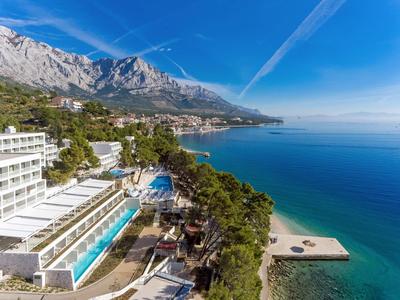 Hotel mit Pool an der Küste, umgeben von Bergen und klarem blauem Meer unter blauem Himmel.