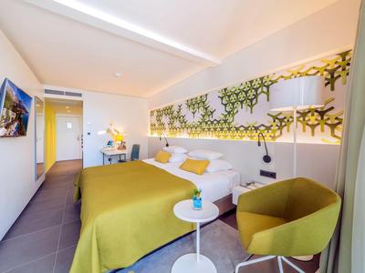 Moderne hotelkamer met groen bed, zithoek, wanddecoratie en tv.