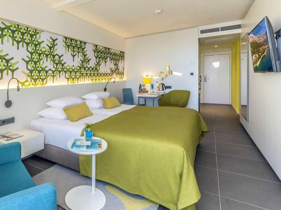 Modern hotelkamer met tweepersoonsbed, groen beddengoed en wanddecoratie van groene planten.