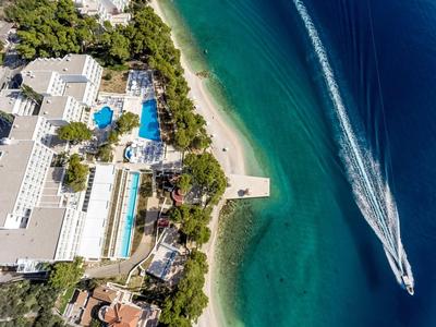 Luchtfoto van een resort met zwembaden naast helderblauwe zee en een boot op het water.
