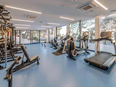Moderner Fitnessraum mit verschiedenen Trainingsgeräten und großen Fenstern mit Bergblick.