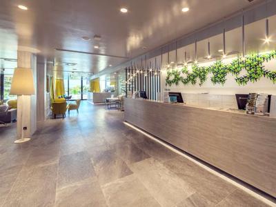 Ruime hotel lobby met een lange receptiebalie en een modern, helder interieur.