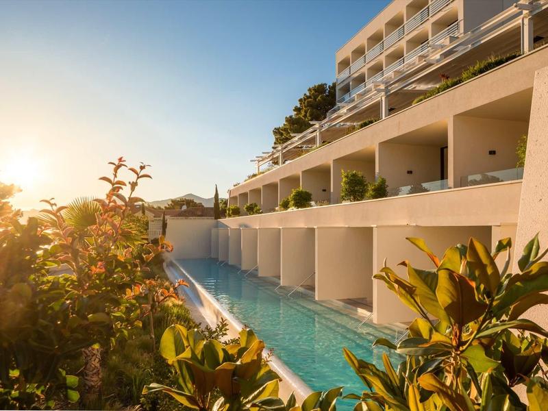 Modern hotel met een lang buitenzwembad omgeven door planten bij zonsondergang.