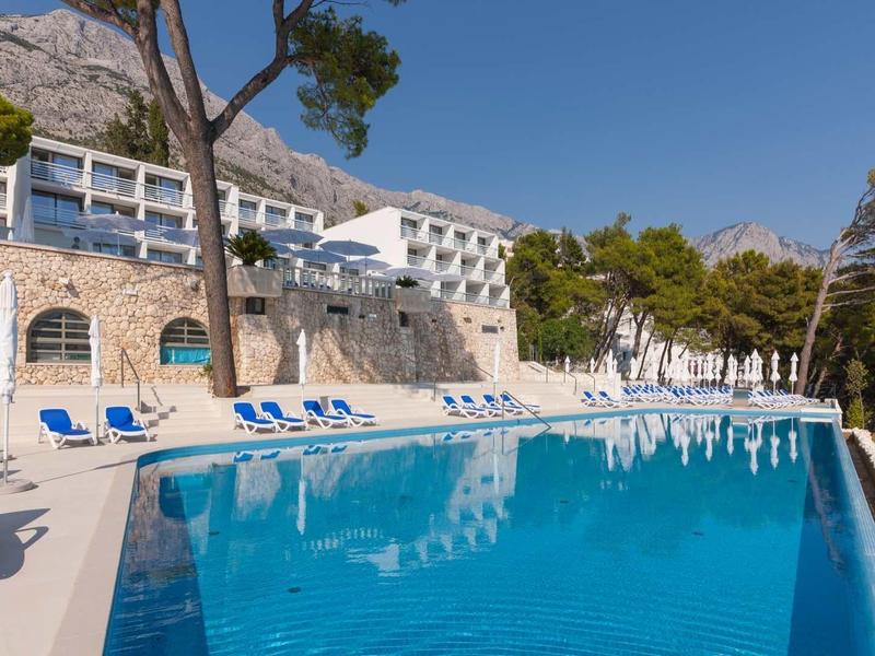 Modern hotel met zwembad, ligbedden en bergen op de achtergrond bij helder weer.