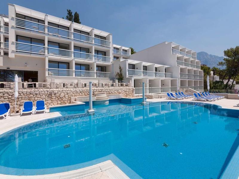 Modern hotelzwembad met blauwe ligstoelen en meerlaagse gebouwen op de achtergrond.