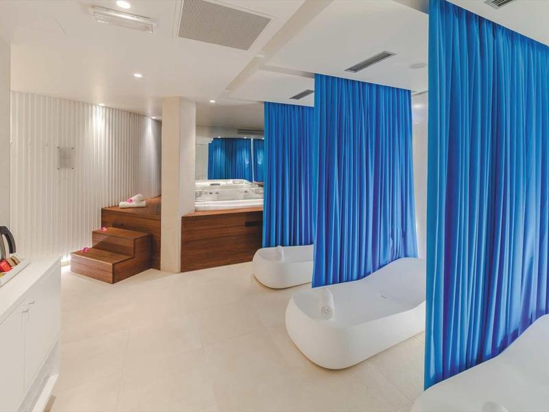Moderne spa met witte ligstoelen, blauwe gordijnen en houten details.