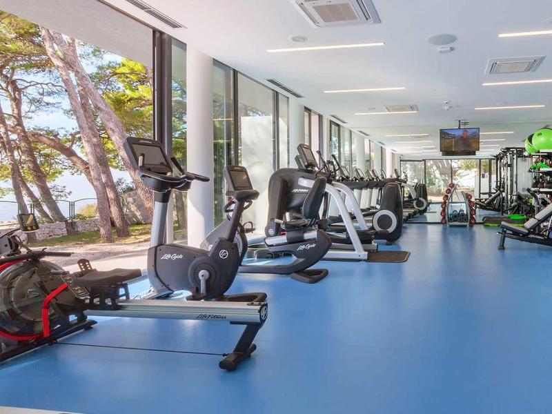 Lichte sportschool met moderne apparatuur en grote ramen met uitzicht op bomen.