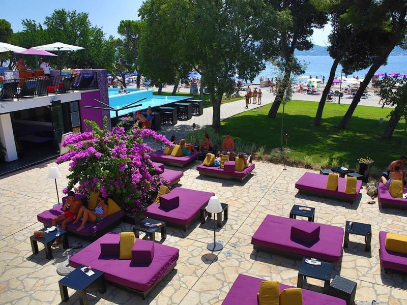 Venkovní posezení s fialovým čalouněným nábytkem a výhledem na bazén a pláž.