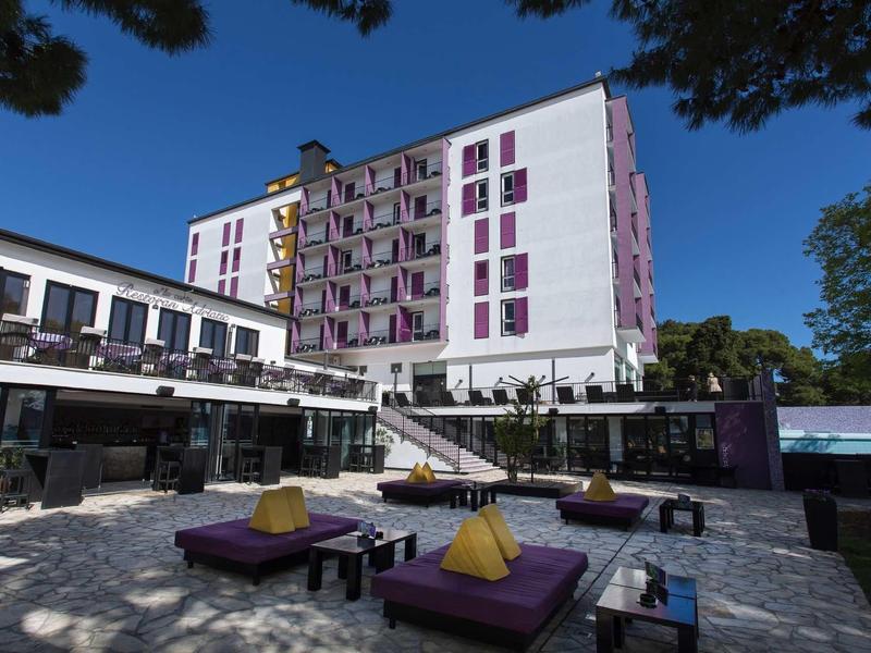 Moderní hotelový komplex s venkovním nábytkem a osvětleným bazénem za denního světla.