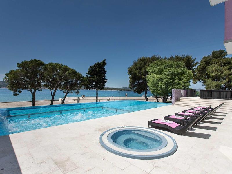 Moderní bazénová oblast s lehátky a vířivkou s výhledem na moře.