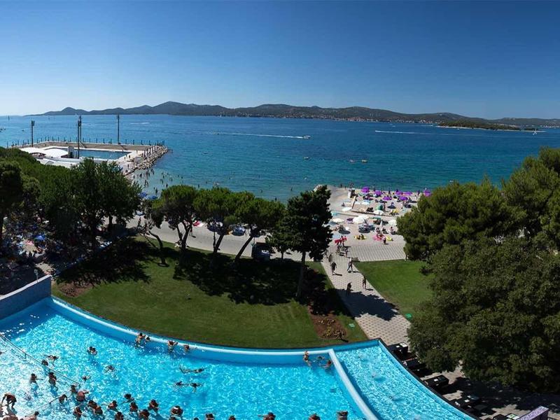 Výhled z balkonu na bazén, pláž a moře pod modrou oblohou.