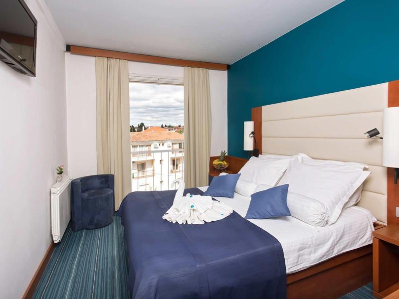 Hotelkamer met tweepersoonsbed, blauw beddegoed, balkon en aan de muur gemonteerde tv.