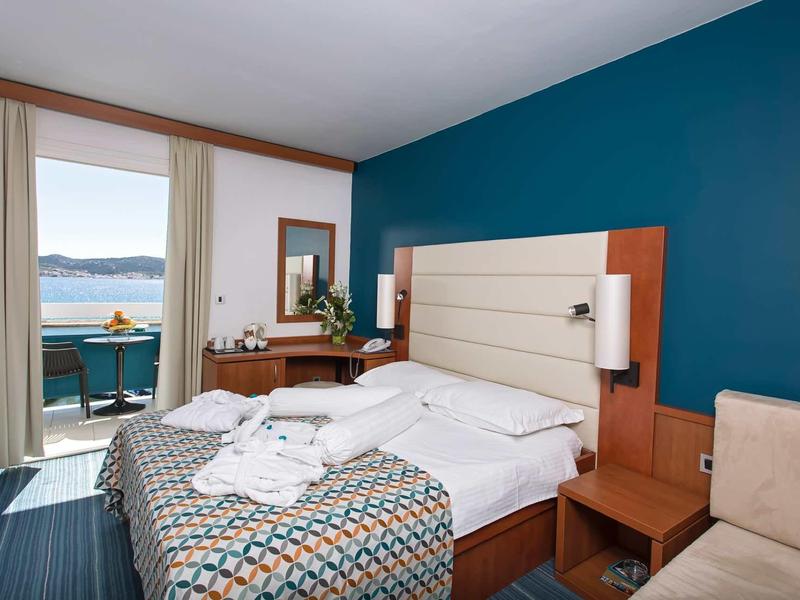 Hotelkamer met tweepersoonsbed, bureau, balkon en uitzicht op water.