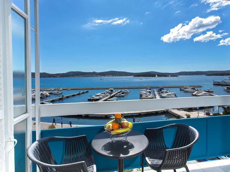 Balkon met tafel, twee stoelen en fruitschaal met uitzicht op jachthaven en kalme zee.