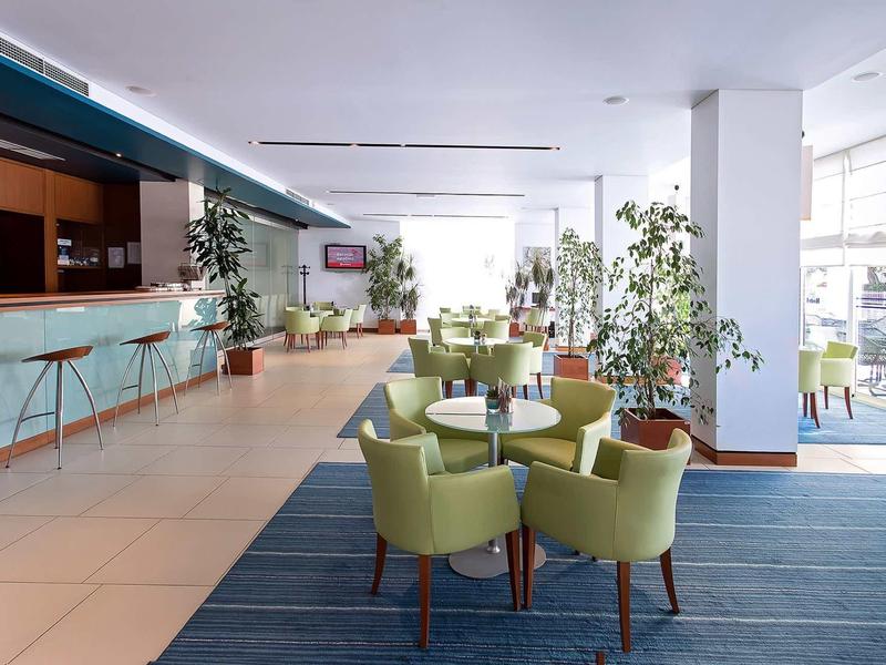 Moderne hotellounge met groene stoelen, bar en grote ramen.