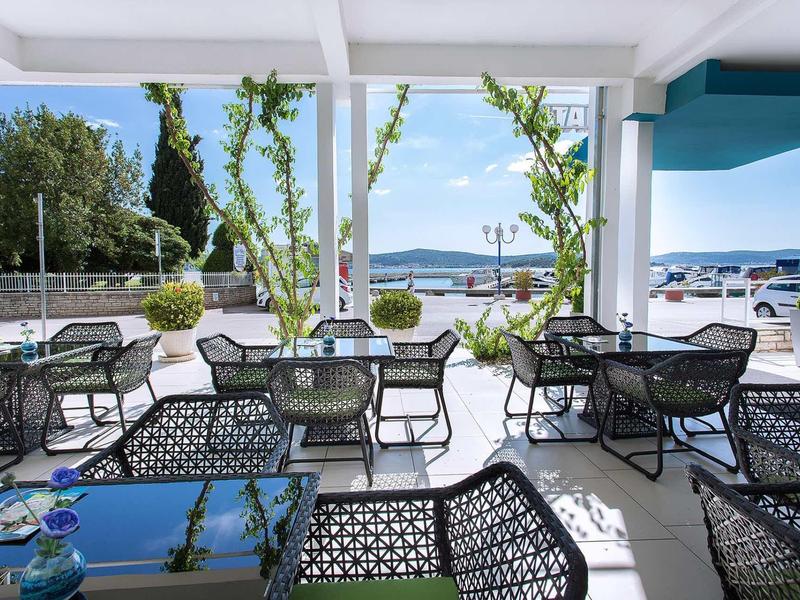 Open buitenruimte met zwarte rotan stoelen en tafels met uitzicht op water en boten.