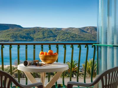 Balcone con piccolo tavolo, due sedie e ciotola di frutta con vista su lago e colline verdi.
