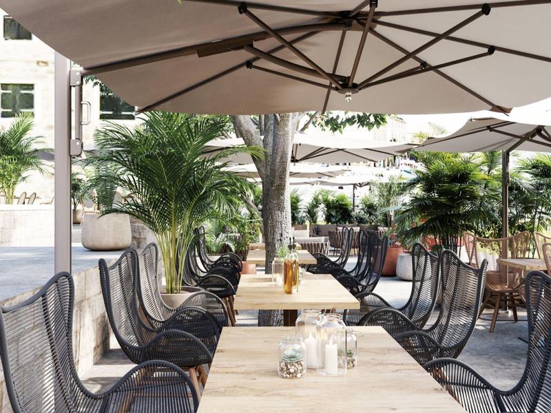 Buitenrestaurant met schaduwrijke tafels, stoelen en tropische planten rondom.