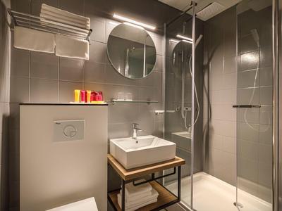 Baño moderno con lavabo cuadrado, espejo redondo y ducha con mampara de vidrio.