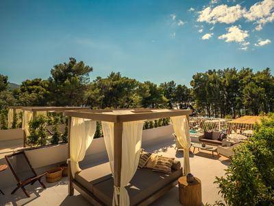 Terraza soleada de hotel con camas, sillones y árboles verdes bajo cielo azul.