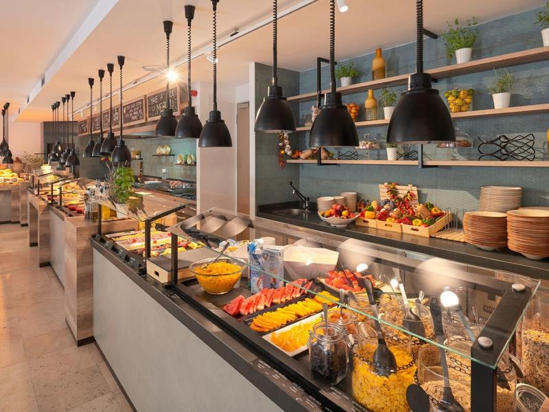 Buffet de desayuno con variedad de platos y luces colgantes en un comedor de hotel.