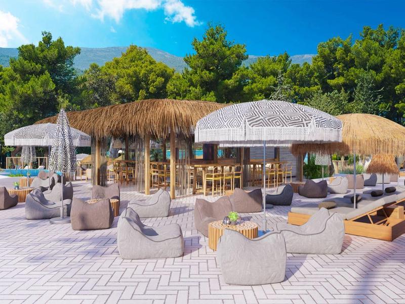 Bar al aire libre con asientos y sombrillas en un entorno verde y soleado en la playa.