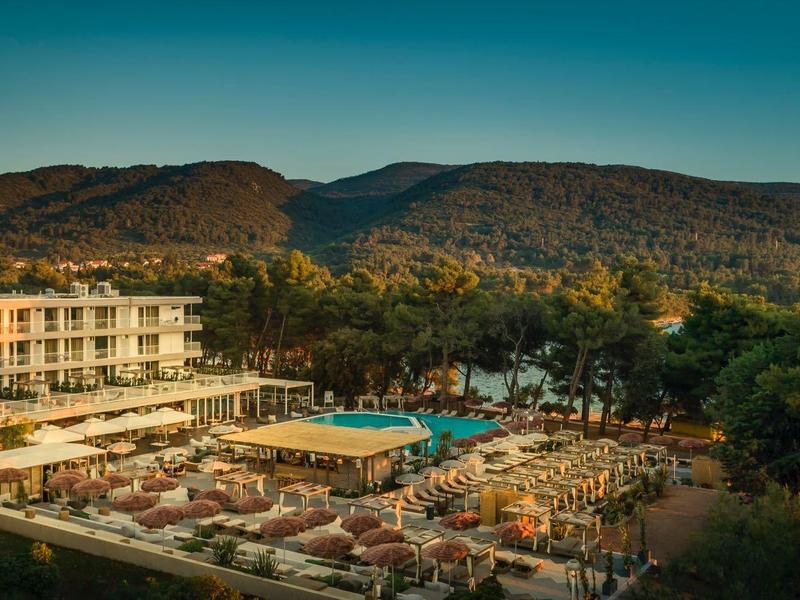 Hotel con gran piscina y tumbonas en un paisaje verde rodeado de colinas.
