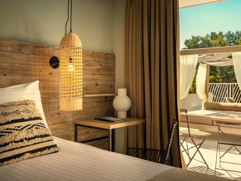 Habitación de hotel elegante con pared de madera, lámpara de mimbre y terraza con vistas verdes.