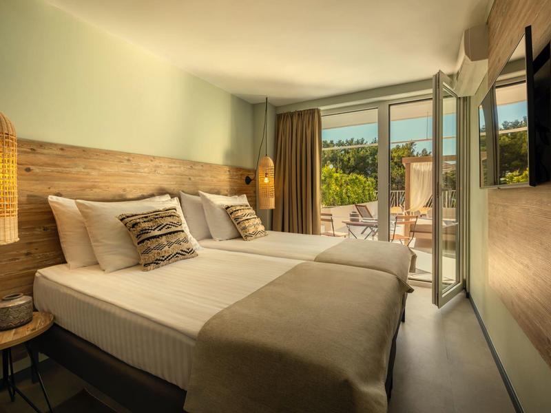 Habitación de hotel acogedora con cama doble, detalles de madera y acceso a terraza con vista al jardín.