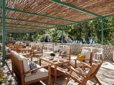 Sonnige Hotelterrasse mit Holzmöbeln, Sitzkissen und Blick auf einen grünen Garten.
