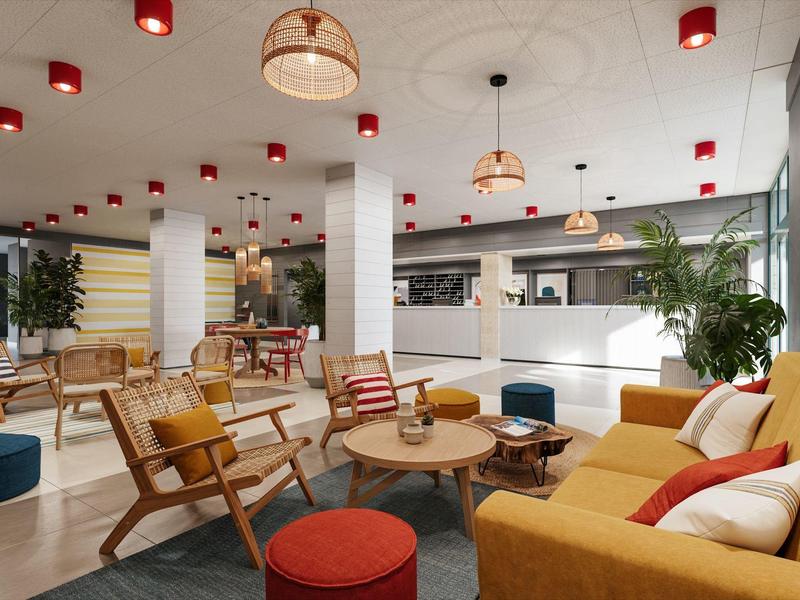 Helles, modernes Café mit gelben Sofas, Holzstühlen, runden Tischen und roten Lampen an der Decke.