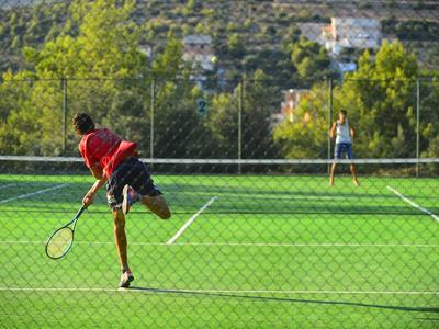 Zwei Personen spielen Tennis auf einem Außenplatz, umgeben von Natur und Hügeln.