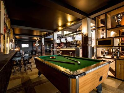 Ein stilvoller Billardraum mit Holzregalen, warmem Licht und einem grünen Billardtisch im Mittelpunkt.