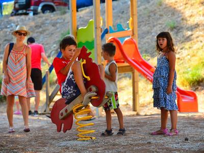 Kinder spielen auf einem Spielplatz mit buntem Klettergerüst und Rutsche im Sonnenschein.