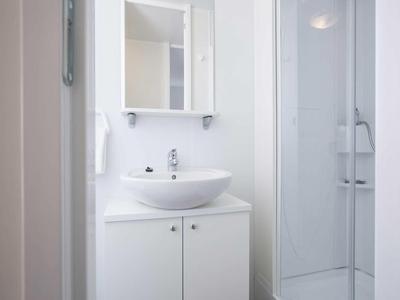 Kompaktes, weißes Badezimmer mit runder Waschschüssel, Spiegel und Duschkabine in hellem Raum.