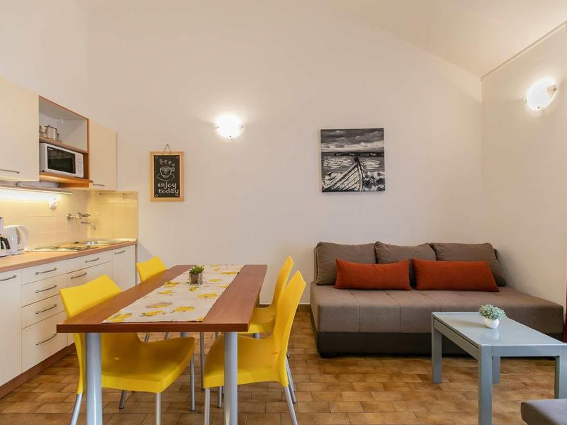 Moderner Wohnraum mit gelben Stühlen, grauem Sofa, Holztisch und offener Küchenzeile.