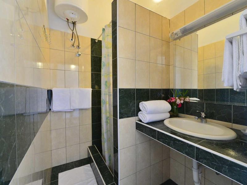 Kleines modernes Badezimmer mit hellen Fliesen, grünem Akzent, Waschbecken und Handtüchern.