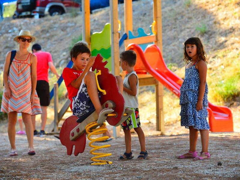 Kinder spielen auf einem Spielplatz mit buntem Klettergerüst und Rutsche im Sonnenschein.
