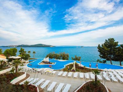 Hotelpool mit Liegestühlen neben dem Meer unter blauem Himmel mit Wolken.