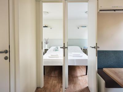 Blick durch eine zweiflügelige Glastür auf zwei Einzelbetten in einem hellen Hotelzimmer.