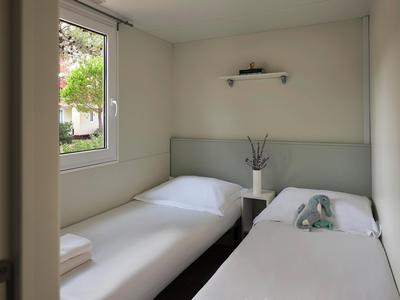 Hell eingerichtetes Hotelzimmer mit zwei Einzelbetten, Fenster mit Blick ins Grüne, weißer Wand und minimaler Dekoration.