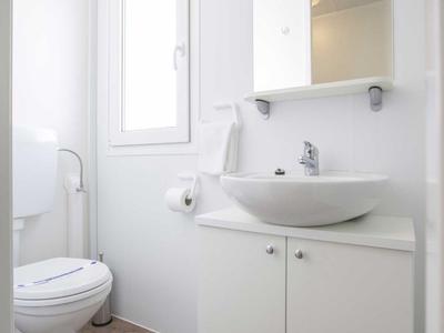 Kleines modernes Badezimmer mit Toilette, Waschbecken und Spiegel über weißem Schrank.