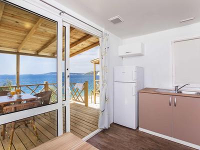 Helle Küche mit kleinem Spülbecken, Kühlschrank und Blick auf überdachte Terrasse mit Meerblick.