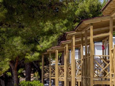 Reihe von Holzbalkonen an einem Haus, umgeben von grünen Bäumen bei Sonnenschein.