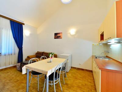 Heller Raum mit Esstisch, weißen Stühlen, blauen Vorhängen, Sofa und moderner Küchenzeile.