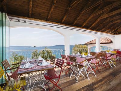 Überdachte Terrasse mit bunten Stühlen und Tischen mit Blick auf das Meer und die Inseln.