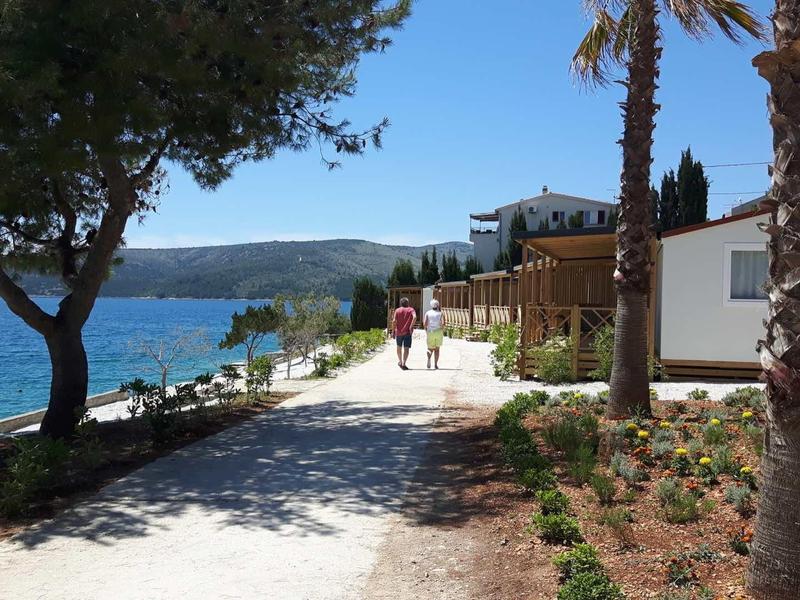Küstenweg mit Bäumen, Palmen und Haus am blauen Meer unter klarem Himmel.